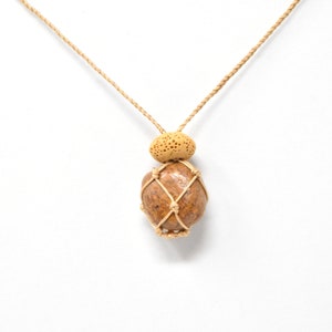 May include: A brown stone pendant with a beige cord necklace. The stone is wrapped in a beige cord net.