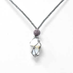 May include: A white opal stone wrapped in a gray macrame net with a gray lava bead on a gray braided cord necklace.