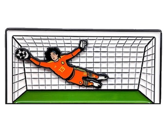 May include: A black and white enamel pin of a soccer player in an orange uniform diving to make a save in a soccer goal. The player is wearing a number 13 on their jersey.