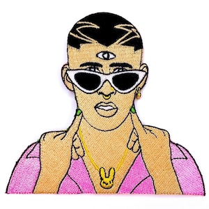 May include: Embroidered patch featuring a cartoon portrait of a person with black hair, a third eye, and sunglasses. The person is wearing a pink shirt and a gold chain with a yellow rabbit pendant. The patch has a white background.