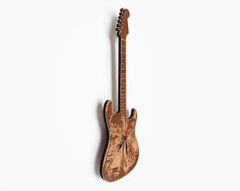 Puede incluir: Un reloj de pared de madera con forma de guitarra. El reloj tiene un acabado marrón con un diseño grabado detallado en el cuerpo. Las manecillas del reloj son negras y rojas. El reloj de guitarra está montado en una pared blanca.