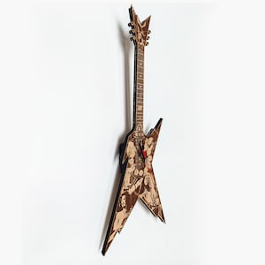 Puede incluir: Una guitarra eléctrica marrón con un cuerpo negro en forma de estrella y una pala negra. La guitarra está decorada con un patrón de imágenes en blanco y negro. La guitarra está colgada en una pared blanca.