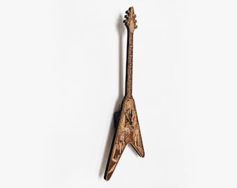 Puede incluir: Una guitarra de madera en forma de V con intrincadas tallas y un diseño detallado. La guitarra es marrón con un mástil largo y seis clavijas de afinación. El cuerpo presenta una ilustración detallada con varias figuras.