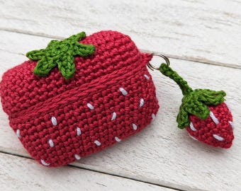 May include: A red crochet strawberry-shaped case with white seed details and a green leaf top. A matching strawberry charm hangs from a metal ring. The case is designed to hold small items.