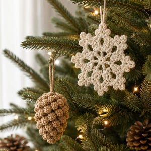 May include: Two handmade crochet ornaments hanging from a pine tree. One ornament is a cream-colored six-pointed snowflake with intricate stitching, and the other is a light brown pinecone shape with a textured, bumpy surface made of yarn.
