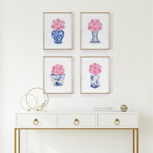 May include: Four framed prints of pink flowers in blue and white porcelain vases. The prints are arranged in a grid pattern on a white wall above a white console table with gold accents.