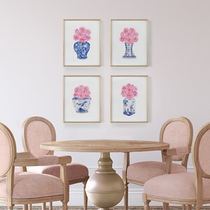 May include: Four framed prints of pink flowers in blue and white porcelain vases. The prints are hanging on a white wall above a round wooden table with four chairs.