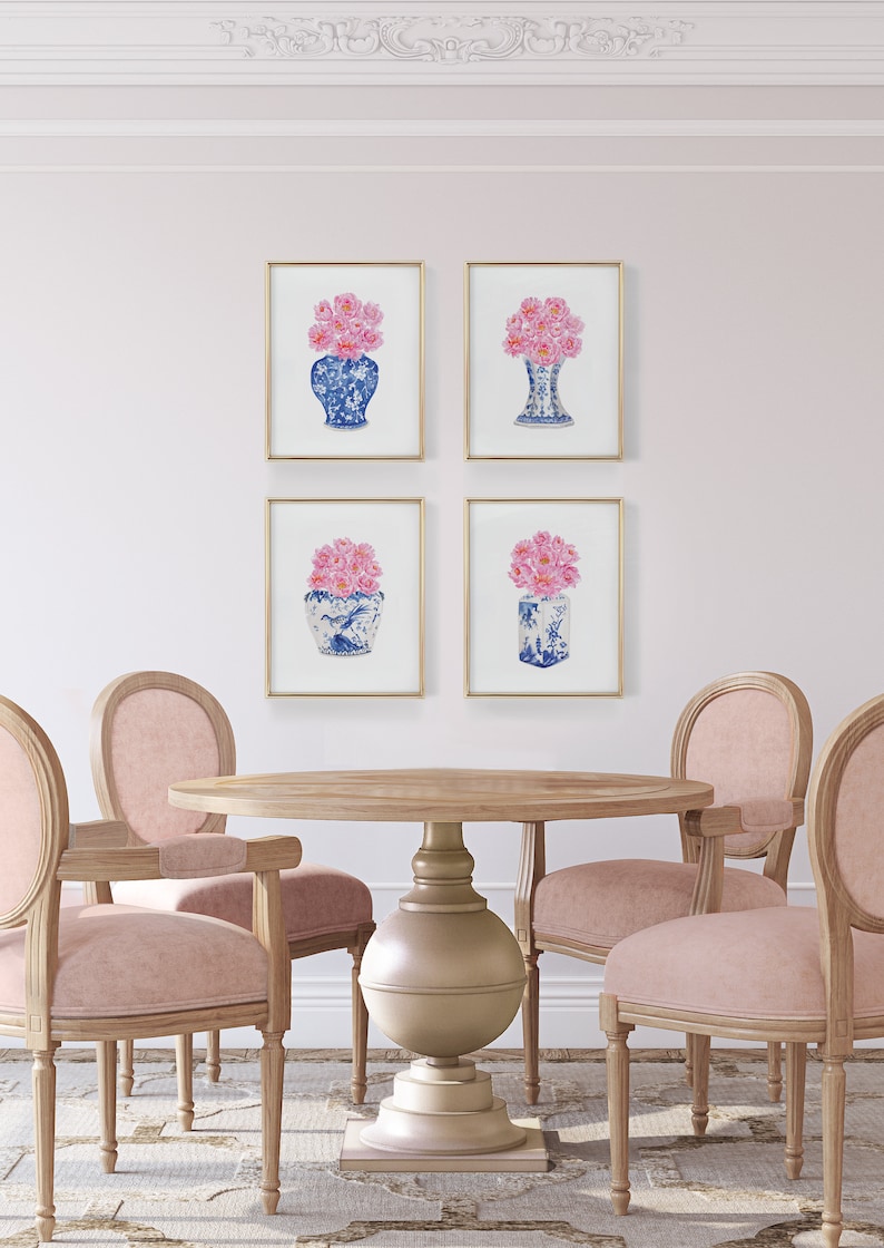 May include: Four framed prints of pink flowers in blue and white porcelain vases. The prints are hanging on a white wall above a round wooden table with four chairs.
