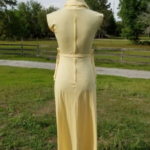 Pode incluir: Um vestido maxi amarelo claro com decote de gola alta e um z&iacute;per nas costas. O vestido tem um la&ccedil;o na cintura e &eacute; sem mangas.