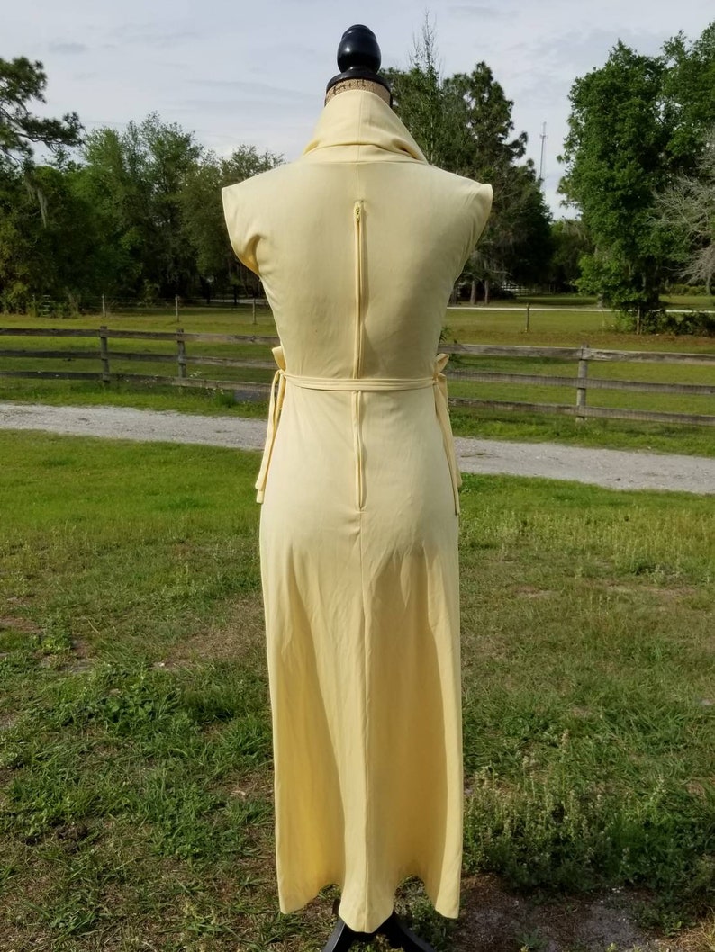 Pode incluir: Um vestido maxi amarelo claro com decote de gola alta e um z&iacute;per nas costas. O vestido tem um la&ccedil;o na cintura e &eacute; sem mangas.