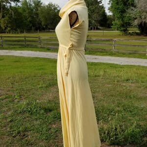 Pode incluir: Um vestido maxi amarelo claro com gola alta e mangas curtas. O vestido tem um la&ccedil;o na cintura e uma saia fluida.