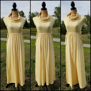 Pode incluir: Um vestido maxi amarelo claro com gola alta e um la&ccedil;o na cintura.