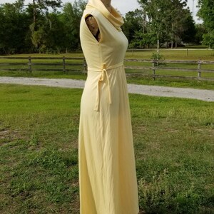 Pode incluir: Um vestido maxi amarelo claro sem mangas com gola alta e um la&ccedil;o na cintura.