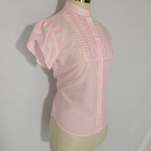 Pode incluir: Uma blusa rosa de manga curta com colarinho franzido e fecho de bot&otilde;es.