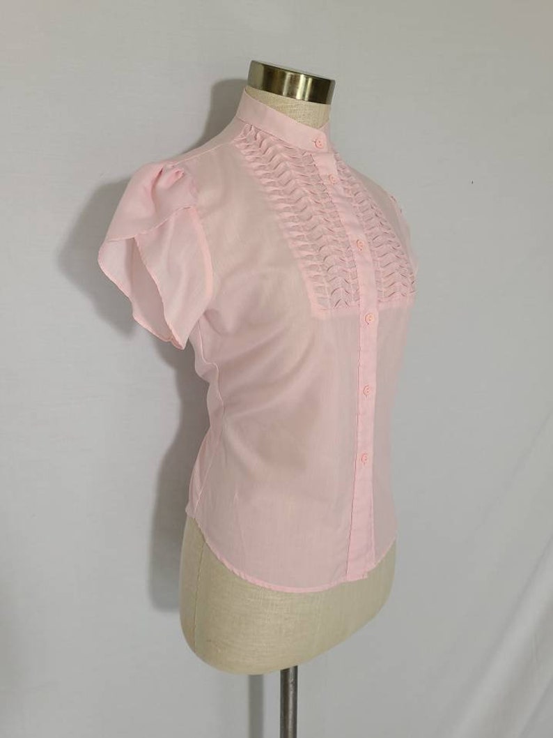 Pode incluir: Uma blusa rosa de manga curta com colarinho franzido e fecho de bot&otilde;es.
