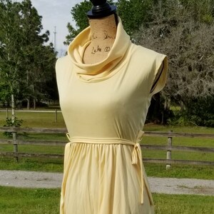 Pode incluir: Um vestido amarelo claro sem mangas com gola alta e um la&ccedil;o na cintura.