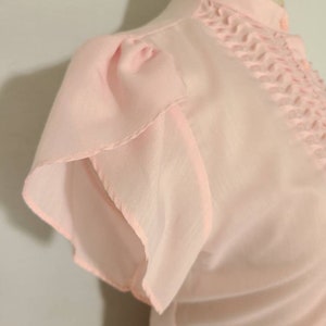 Pode incluir: Uma blusa rosa claro com colarinho franzido e mangas bufantes. A blusa &eacute; feita de um tecido transparente e tem um caimento solto.