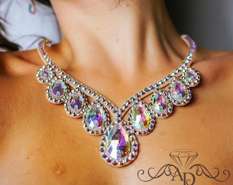 Puede incluir: Un delicado collar de cristal iridiscente con un colgante en forma de lágrima. El collar está hecho de pequeños cristales facetados que están engastados en un metal plateado.