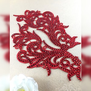 May include: Red rhinestone applique with a floral design. The applique is made of small red rhinestones that are sewn onto a fabric base.