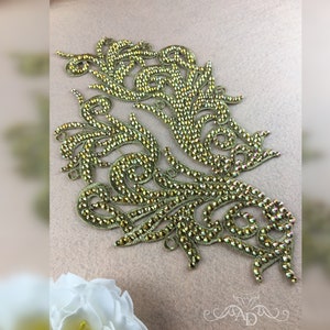 May include: Gold rhinestone applique with a floral design. The applique is made of small, iridescent rhinestones that are sewn onto a fabric base.