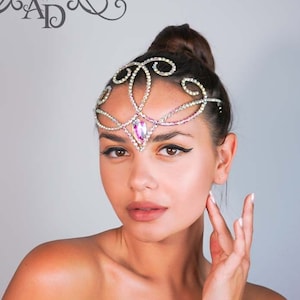 Puede incluir: Una mujer lleva una diadema de cristal plateado y rosa con un diseño delicado y ornamentado. La diadema está hecha de metal y presenta un gran cristal rosa en el centro.