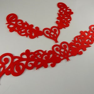 May include: Red felt cutouts in the shape of hearts and swirls. The cutouts are arranged in a decorative pattern.