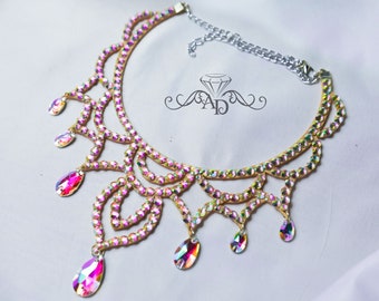 May include: A delicate gold-toned choker necklace with multiple rows of iridescent pink and clear rhinestones. The necklace features a dangling design with teardrop-shaped crystals.