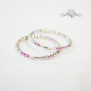 May include: A pair of iridescent hoop earrings with a silver metal base. The hoops are adorned with small, faceted crystals.