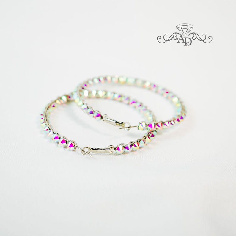 May include: A pair of iridescent hoop earrings with a silver metal base. The hoops are adorned with small, faceted crystals.