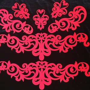 May include: Four red paper cutouts of intricate floral designs on a black background. The designs are symmetrical and feature swirls and loops.