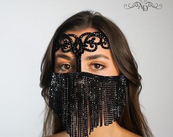 May include: A black beaded face mask with a fringe and a decorative headband. The headband has a floral design.