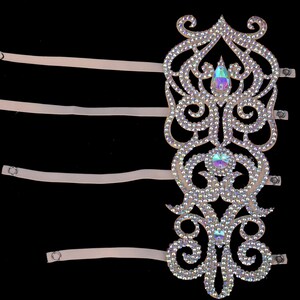 May include: A white, ornate, rhinestone-encrusted arm band with four adjustable straps. The arm band has a delicate, floral design with iridescent rhinestones.