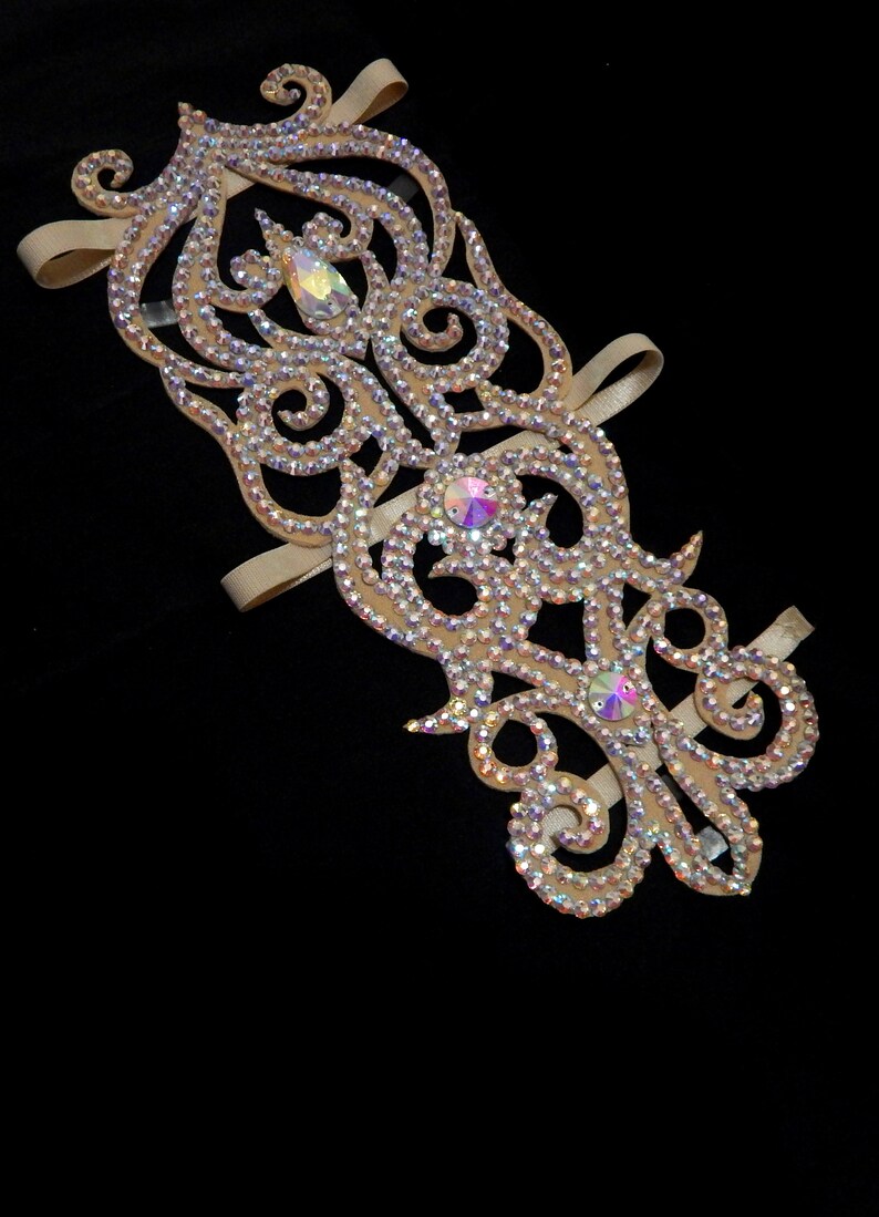 May include: A beige dance arm band with a decorative design featuring swirls and rhinestones.