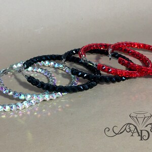 May include: Three pairs of hoop earrings with crystal embellishments. The earrings are in silver, black, and red.