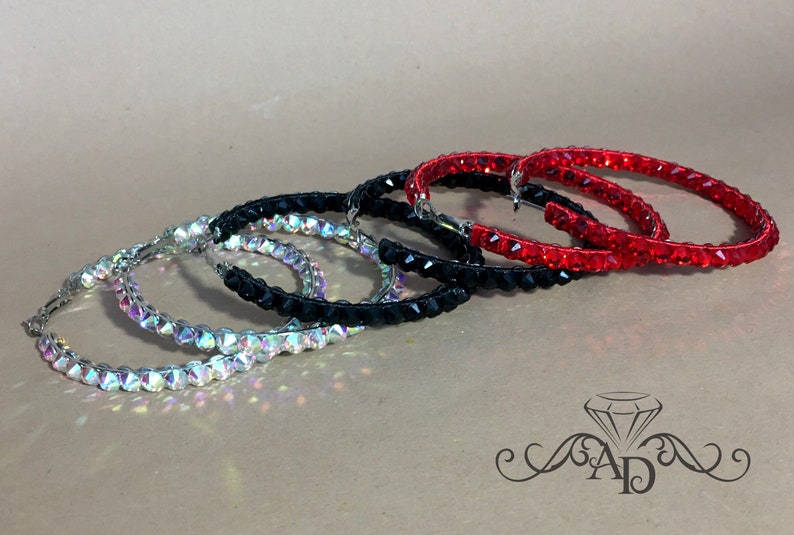 May include: Three pairs of hoop earrings with crystal embellishments. The earrings are in silver, black, and red.