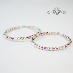 May include: A pair of large, silver hoop earrings with iridescent rhinestones. The earrings are made of metal and have a shiny finish.