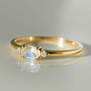 May include: A gold ring with a large oval moonstone and two smaller round diamonds. The ring is on a white surface.