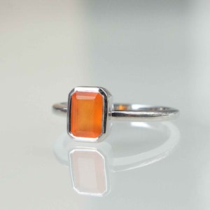 May include: A silver ring with an orange gemstone set in a square shape.