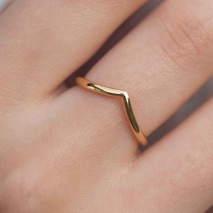 May include: A gold-colored V-shaped ring on a finger.