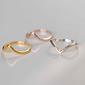 May include: Three simple, minimalist rings in gold, silver, and rose gold. Each ring features a V-shaped design.