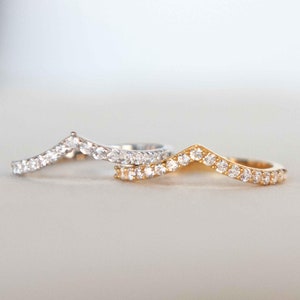 May include: Two delicate chevron shaped rings with a row of small clear cubic zirconia stones. The ring on top is silver and the ring on the bottom is gold.