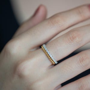 Pu&ograve; includere: Una coppia di anelli sovrapposti indossati su un dito. Il primo &egrave; una sottile fascia in oro composta da una fila continua di piccole perle dorate lucide. Il secondo &egrave; una sottile fascia color argento incastonata con una fila di piccole pietre chiare.