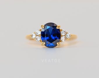 May include: A gold ring with a large, oval-shaped blue sapphire gemstone surrounded by smaller, clear gemstones.