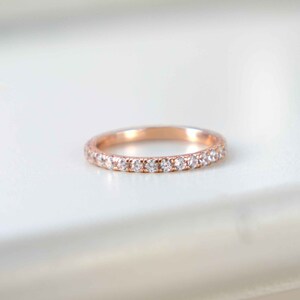 Pu&ograve; includere: Un anello a fascia in oro rosa con una fila di piccole pietre trasparenti a taglio rotondo incastonate lungo la met&agrave; anteriore. Il metallo ha una finitura lucida e le pietre sono disposte in una linea continua, creando un effetto brillante.