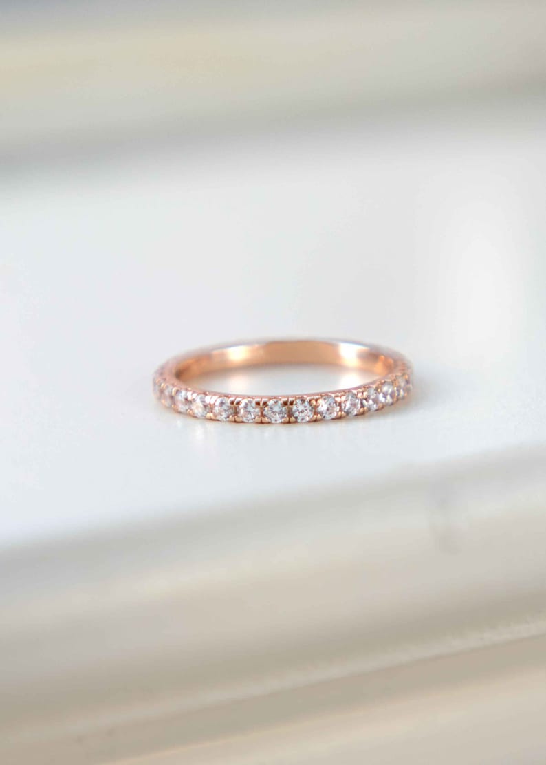 Pu&ograve; includere: Un anello a fascia in oro rosa con una fila di piccole pietre trasparenti a taglio rotondo incastonate lungo la met&agrave; anteriore. Il metallo ha una finitura lucida e le pietre sono disposte in una linea continua, creando un effetto brillante.