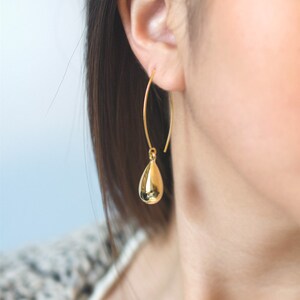 May include: Gold teardrop dangle earrings with a simple, minimalist design. The earrings are made of a thin, delicate wire and feature a small, round teardrop-shaped charm.