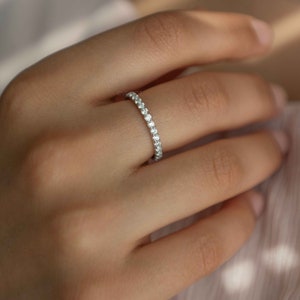 Pu&ograve; includere: Un sottile anello color argento caratterizzato da una fila continua di piccole pietre chiare a taglio rotondo lungo l'intera circonferenza esterna. La fascia in metallo ha una finitura lucida e le pietre sono disposte in modo uniforme.