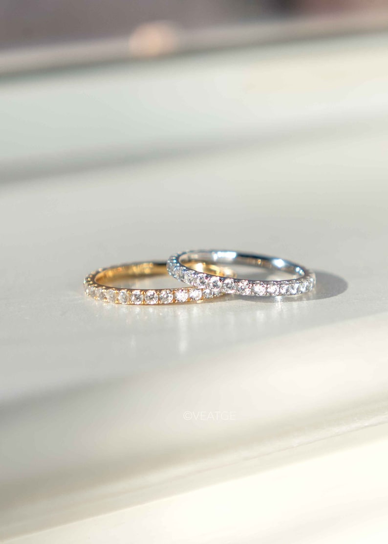 Pu&ograve; includere: Due anelli a giro completo con una fila continua di piccole pietre chiare a taglio rotondo. Un anello &egrave; realizzato in oro giallo, mentre l'altro &egrave; in metallo color argento. La parola OVEATGE &egrave; stampata in piccole lettere chiare vicino agli anelli.
