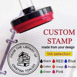 Peut inclure: Un tampon personnalisé avec une poignée noire et rouge est pressé sur un bloc-notes. Le motif du tampon comprend une pile de livres et le texte "FROM THE LIBRARY OF CRISTINA TOALDO". L'image montre également les options de couleur d'encre : noir, rouge, bleu, café, orange, violet, vert et rose.