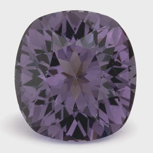 Può includere: Una pietra preziosa viola con taglio a cuscino e superficie sfaccettata che crea un motivo simmetrico a stella di riflessi chiari e scuri. La gemma presenta profonde tonalità viola e bordi geometrici netti sulla faccia superiore.